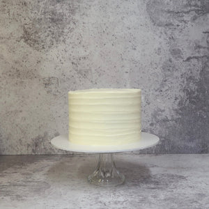 Layer cake covered in cream with lines piped on it, cake on white board, Lemon & Elderflower gin cake