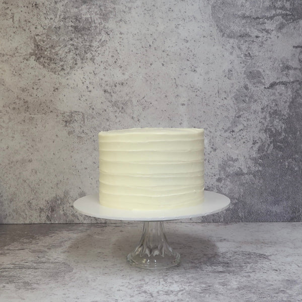 Layer cake covered in cream with lines piped on it, cake on white board, Lemon & Elderflower gin cake