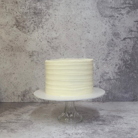 Layer cake covered in cream with lines piped on it, cake on white board, Lemon & Elderflower gin cake